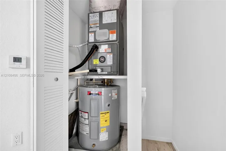 Utility closet featuring a stacked forced-air heating and cooling unit with an integrated water heater and louvered access door