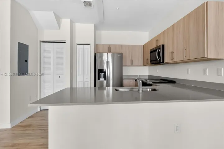Kitchen featuring light-finish cabinetry, stone-surface countertops, stainless steel appliances, and wood-finish flooring
