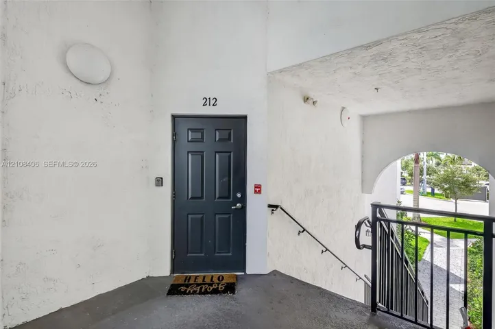 Exterior entry featuring a dark-toned paneled door, textured wall finish, and an arched entryway with a black metal railing