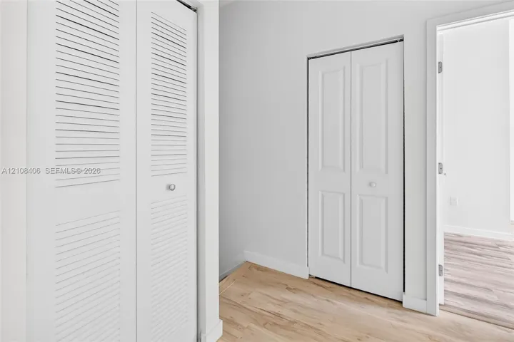 White bi-fold doors with louvered panels, white paneled doors, and light-toned wood-finish flooring