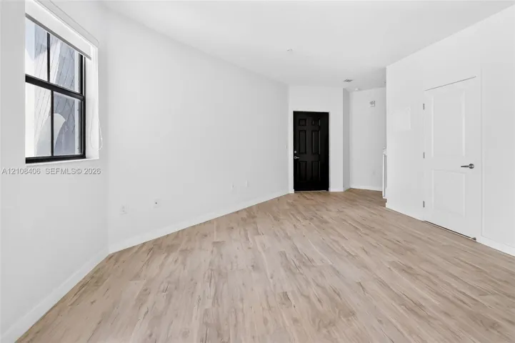 Neutral-toned wood-finish flooring, multi-pane window with black frame, solid-core black interior door, and white panel door