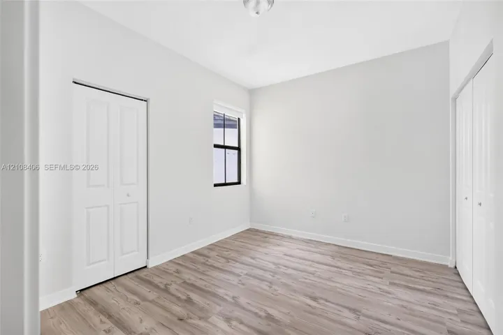 Neutral interior featuring wood-finish flooring, two sets of white paneled bi-fold closet doors, and a window with a black frame