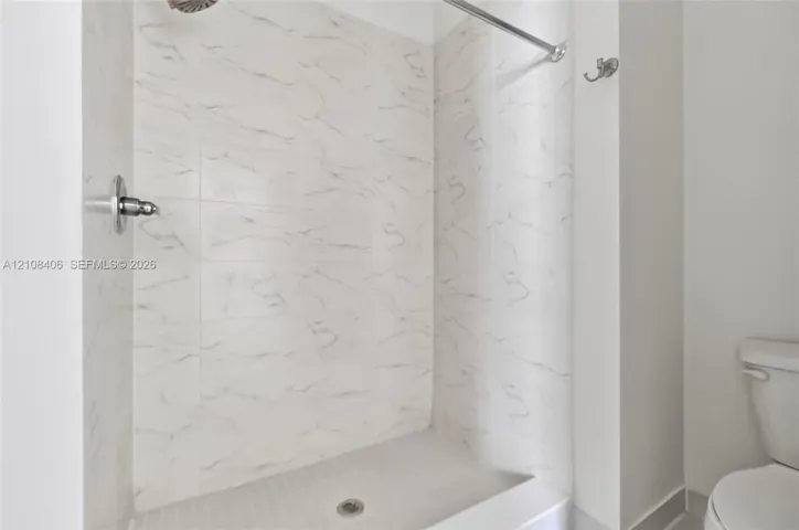 Shower enclosure featuring white tile with grey veining, a wall-mounted shower head, a chrome shower valve, a metal shower curtain rod, and a wall-mounted hook