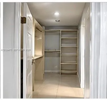 Walk-in closet featuring light-toned tile flooring, built-in open shelving units, and integrated hanging rods