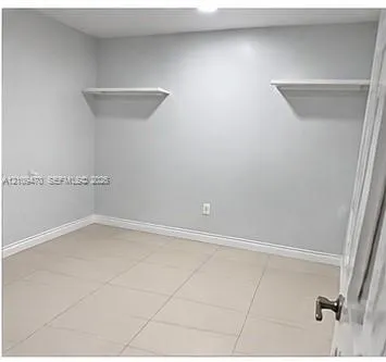 Room featuring neutral-toned tile flooring, light gray walls, and dual built-in wall-mounted shelves