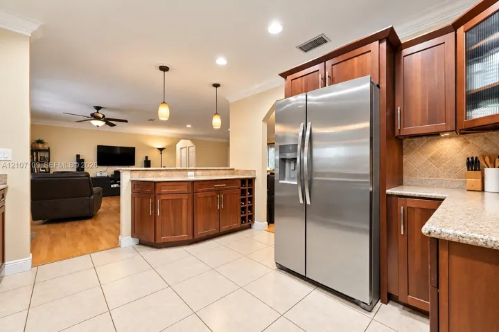 Kitchen featuring wood cabinetry, stone countertops, stainless steel refrigerator, built-in wine rack, and pendant lighting