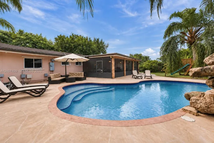 In-ground swimming pool featuring built-in stairs, decorative stone accent, concrete paver decking, and a screened-in lanai