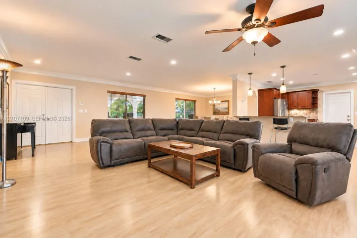 Open-concept area featuring wood-finish flooring, recessed lighting, a ceiling fan with integrated light fixture, and crown molding