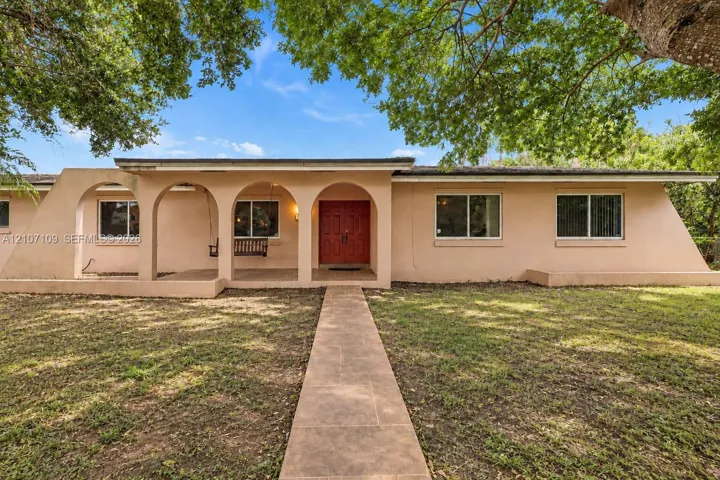Stucco exterior featuring a covered front porch with arched masonry supports, double-door entryway, and a paved walkway