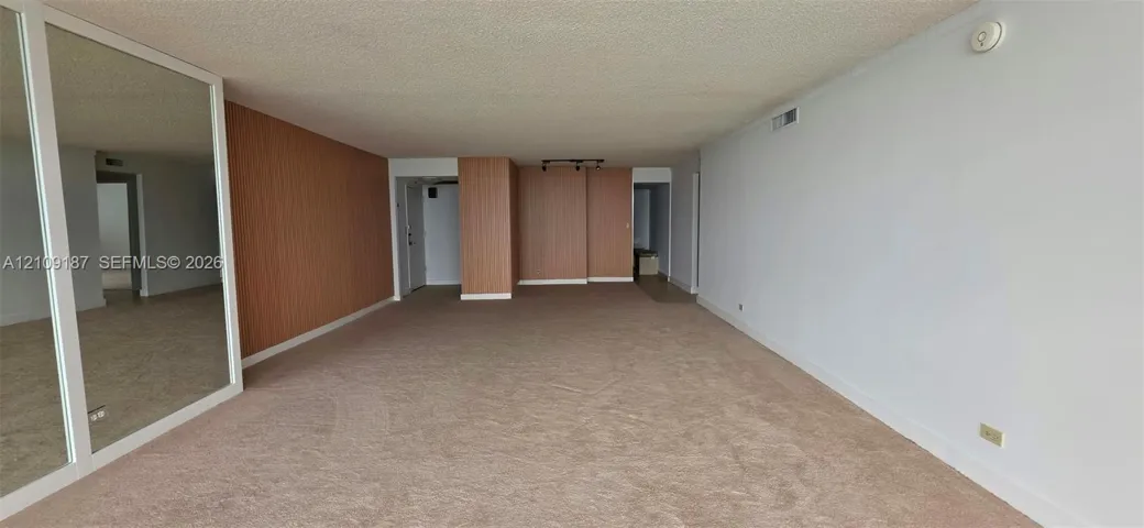 Spacious dinning-living room featuring floor-to-ceiling mirrored panels and wood-finish wall paneling.