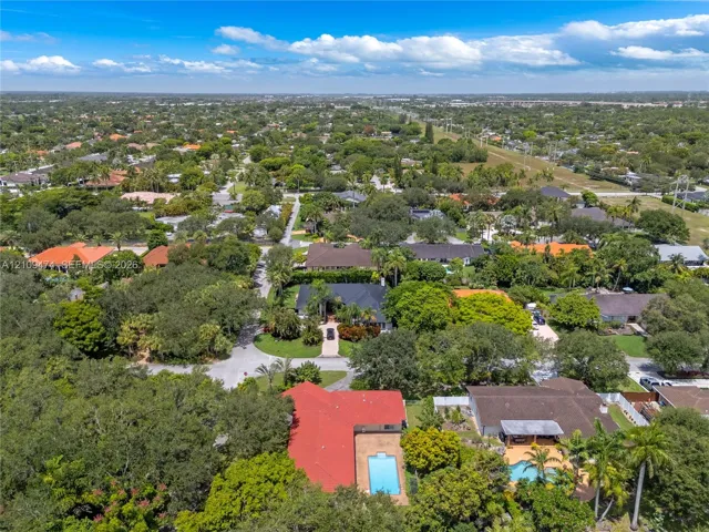 Aerial perspective showcasing a residential lot featuring a red-tiled roof, an inground swimming pool, mature perimeter landscaping, and a paved driveway