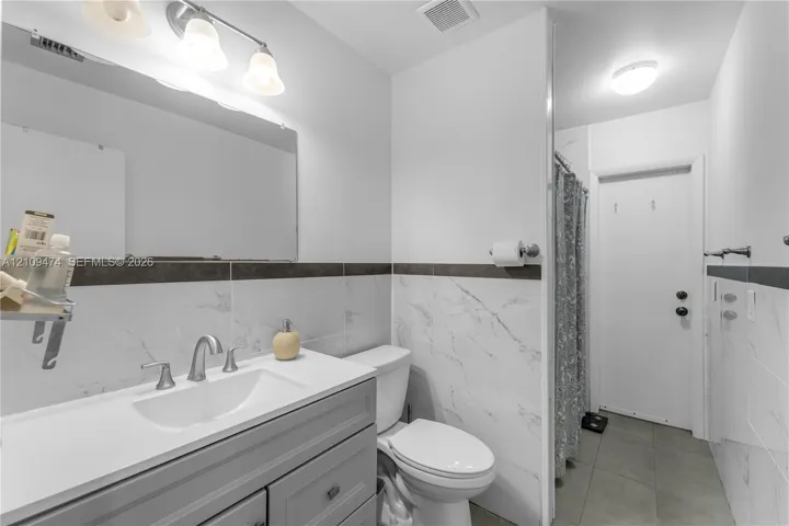 Bathroom featuring a grey vanity with a white countertop, wall-to-wall mirror, three-light fixture, and wall tiles with a dark accent border