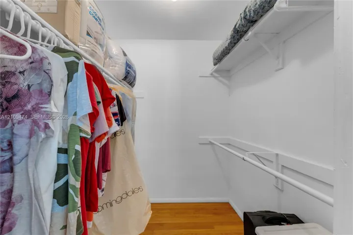 Reach-in closet featuring wood-finish flooring and dual-level white metal shelving and hanging rods