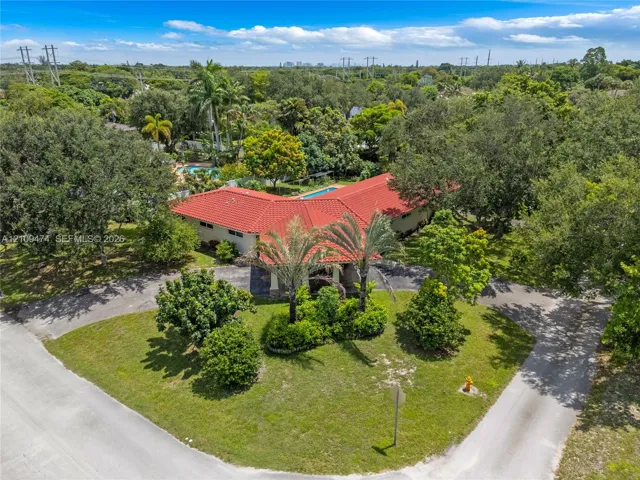 Single-story residence featuring a red tile roof, expansive corner lot, paved circular driveway, mature palm landscaping, and in-ground pool