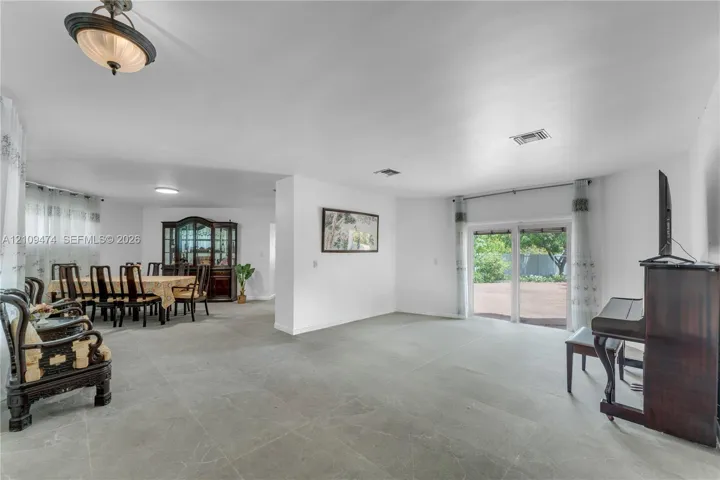 Open-concept interior featuring large-format tile flooring, sliding glass doors, neutral wall color, and a semi-flush mount light fixture