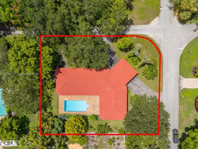 Corner lot featuring a red tile roof, inground swimming pool, paved patio, and mature tree canopy