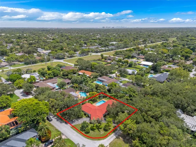 Aerial perspective featuring a red tile roof, an in-ground swimming pool, a sprawling lot with mature trees, and a concrete driveway