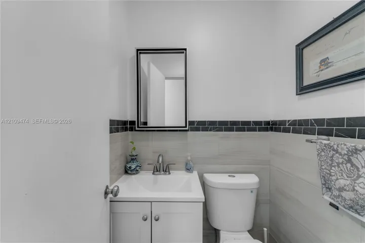 White vanity with a rectangular sink, brushed nickel faucet, wall-mounted mirror with a black frame, and gray stone-finish wall tile featuring a black linear tile border