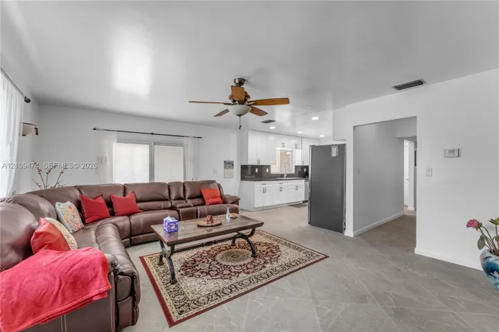Open-concept main room featuring neutral tile flooring, white cabinetry, a ceiling fan with integrated lighting, and sliding glass patio doors