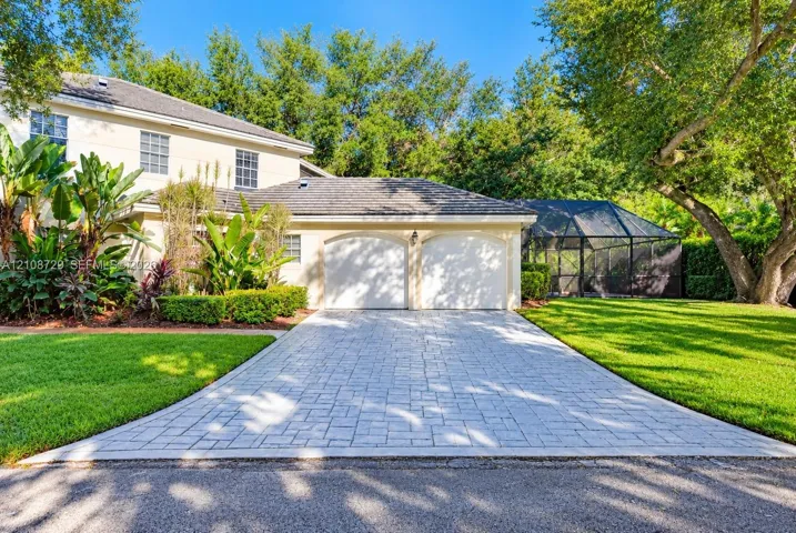 Two-story exterior featuring a stone-paver driveway, a two-car garage with arched entries, and a screened-in lanai