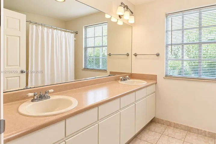 Bathroom upstairs. Dual-sink vanity upstairs with solid-surface countertop, full-width wall mirror, tiled flooring, and chrome hardware fixtures