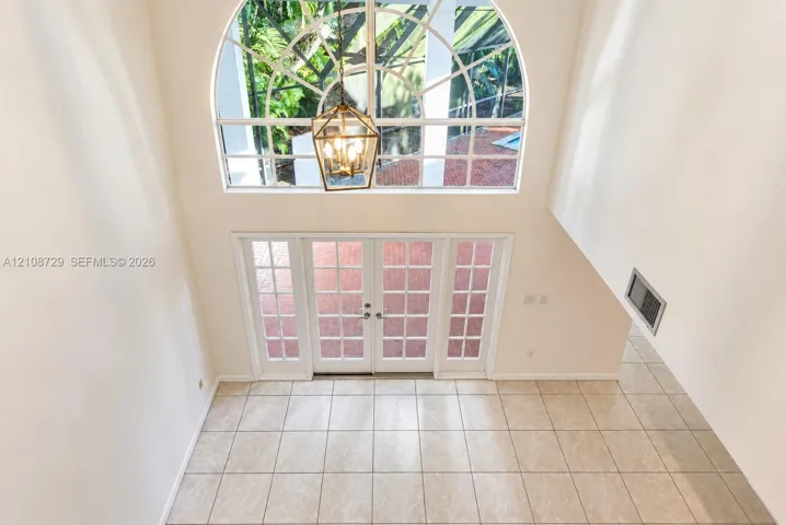 View of family room from upstairs. Double-height ceiling featuring an arched clerestory window, white French doors with glass panes, geometric metal pendant lighting, and ceramic tile flooring