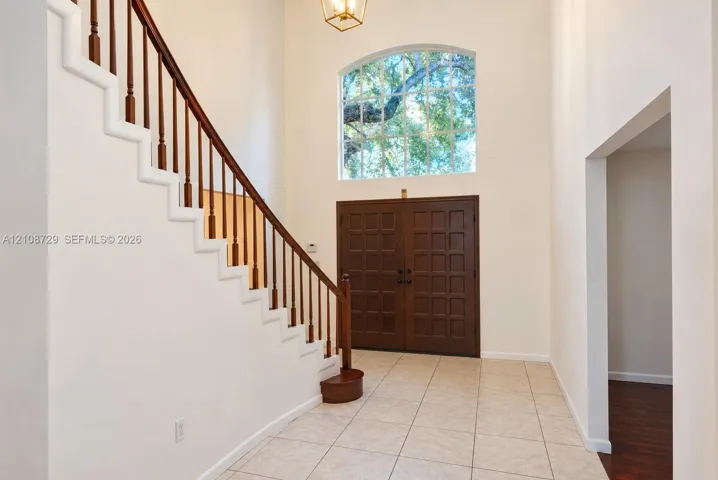 Double-height foyer featuring ceramic tile flooring, a staircase with wood railings, a large arched window, and double entry doors