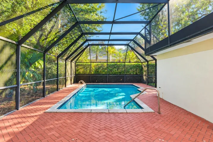 Screened enclosure featuring a rectangular swimming pool, herringbone-patterned brick paver decking, and metal handrails