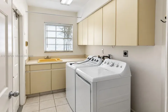 Laundry room featuring ceramic tile flooring, ample cabinetry, solid-surface countertop with an integrated drop-in sink, and window with built-in blinds
