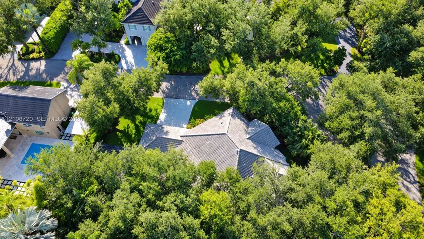 Aerial perspective featuring a tile roof, paved driveway, swimming pool with stone-tiled decking, and mature canopy trees