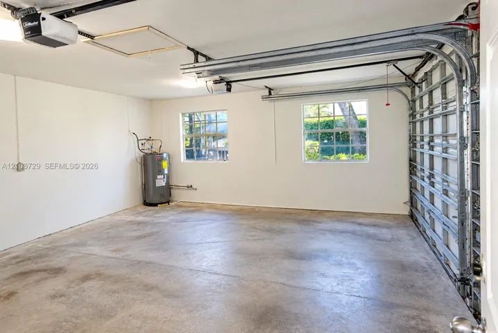 Multi-car garage featuring a concrete floor, two grid-pattern windows, an automated door opener, and a ceiling access panel