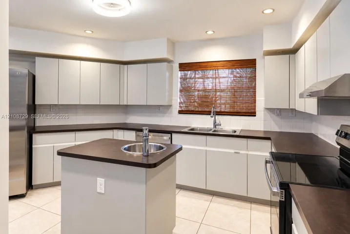 Kitchen featuring matte cabinetry, dark countertops, a center island with a secondary sink, stainless steel appliances, and tile flooring