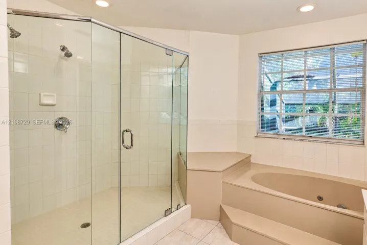 Walk-in shower with a glass enclosure, dual shower heads, recessed lighting, and a built-in jetted tub with a tiered surround
