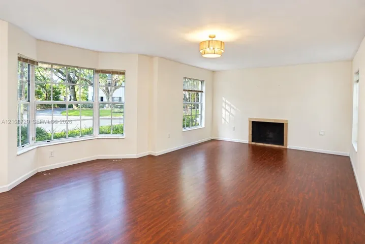Open interior space featuring wood laminated fflooring, a bay window, a recessed fireplace with a stone surround, and a drum-style pendant light