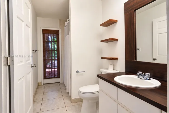 Bathroom featuring a door with access to the pool, white vanity with a dark wood-finish countertop, integrated oval sink, floating wood shelving, and tile flooring