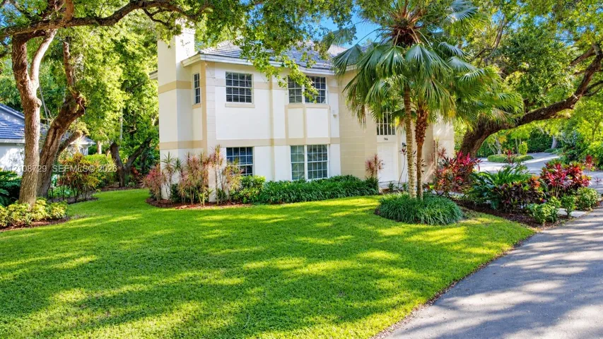 Two-story stucco exterior featuring a chimney, multi-pane windows, mature trees, and landscaped gardens