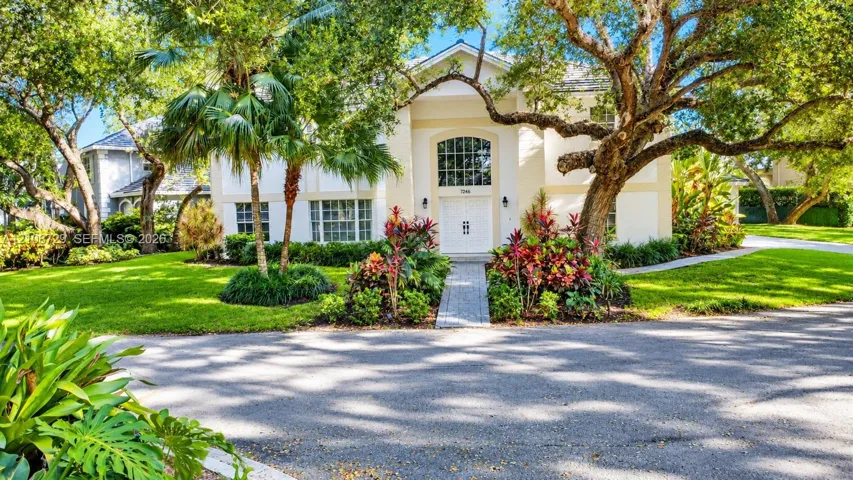 Two-story exterior featuring a high-pitched roofline, an arched transom window above double entry doors, a stone-paver walkway, and mature landscaping