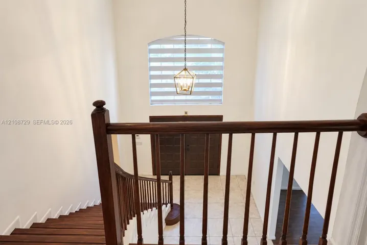 Double-height entryway featuring a wood-finish staircase with a turned-wood railing, arched window, metal-frame pendant lighting, and a set of paneled double front doors