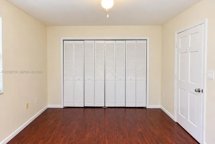 Bedroom upstairs. Interior space featuring wood-laminated flooring, floor-to-ceiling white louvered bifold closet doors, a six-panel interior door, and overhead lighting