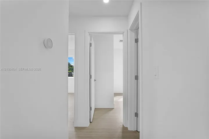 Neutral-toned interior featuring wood-finish flooring, white walls, recessed ceiling lighting, a mounted smart thermostat, and interior swinging doors