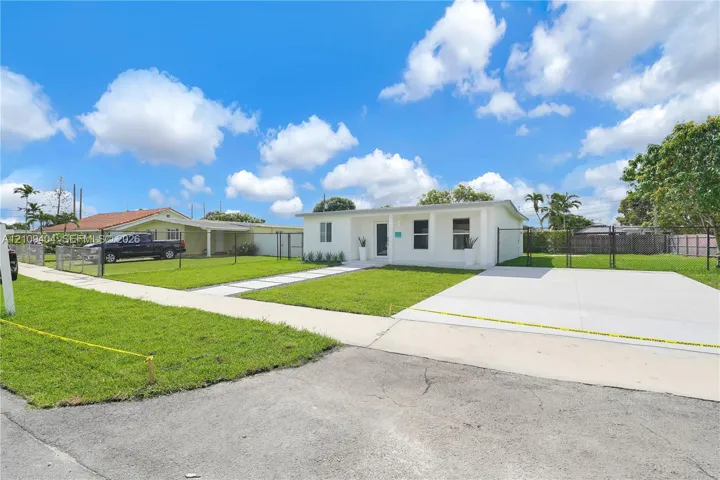Single-story residence featuring a clean white exterior, recessed entry, concrete driveway, and chain-link perimeter fencing