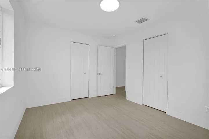 Neutral interior space featuring wood-finish flooring, crisp white wall finishes, two-panel interior doors, and dual bi-fold closet doors