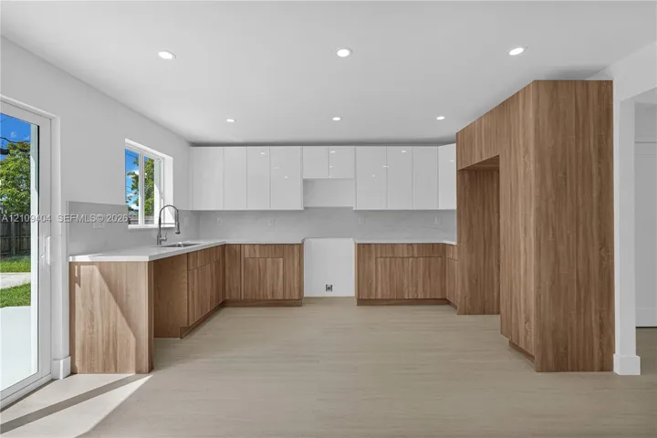 Kitchen featuring two-tone cabinetry, wood-finish lower cabinets, high-gloss white upper cabinets, stone-surfaced countertops, and recessed lighting