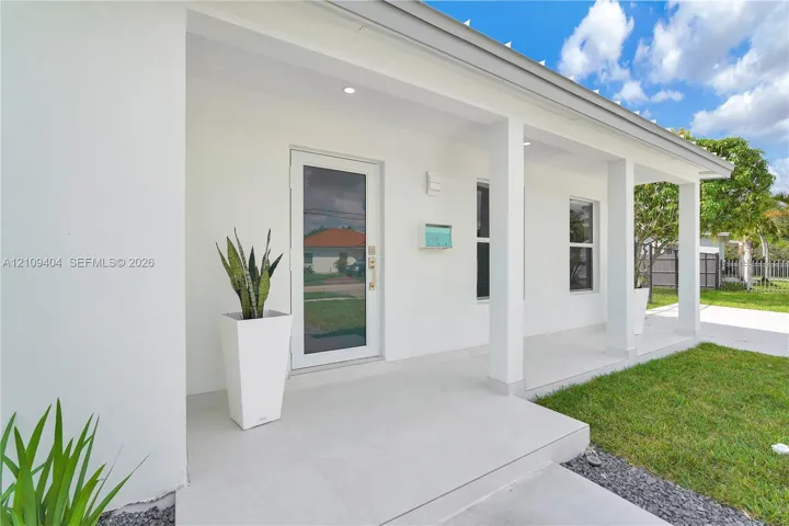 Covered front porch featuring smooth concrete flooring, square support columns, recessed ceiling lighting, and a glass-paneled entry door