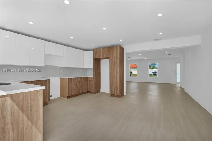 Kitchen featuring high-gloss white upper cabinetry, wood-finish base cabinetry, stone-patterned backsplash, recessed lighting, and wood-finish flooring