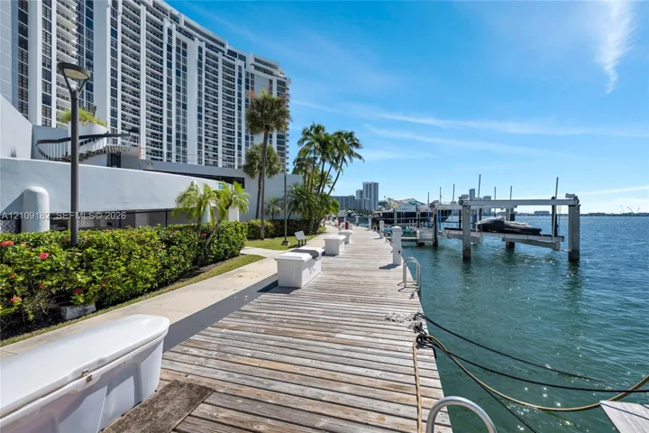 Waterfront wooden dock featuring integrated boat slips, mooring cleats, and proximity to maintained landscaping and palm trees