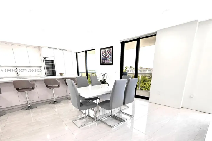 Open kitchen featuring flat-panel cabinetry, light-toned waterfall countertop, built-in wine refrigeration, large-format tile flooring, and floor-to-ceiling sliding glass doors