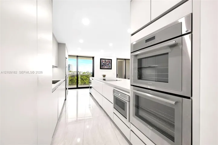 Sleek kitchen featuring flat-panel cabinetry, light-toned stone-surface countertops, built-in stainless steel double wall ovens, a built-in microwave, and polished tile flooring