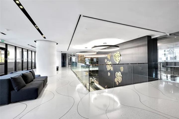 Polished white flooring featuring dark linear patterns, glass partition railing, circular pendant lighting, and a dark accent wall