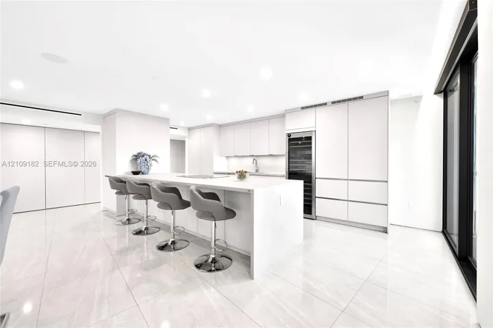 Open kitchen featuring flat-panel cabinetry, a central island with a solid-surface countertop, built-in wine refrigeration, and polished stone-finish flooring